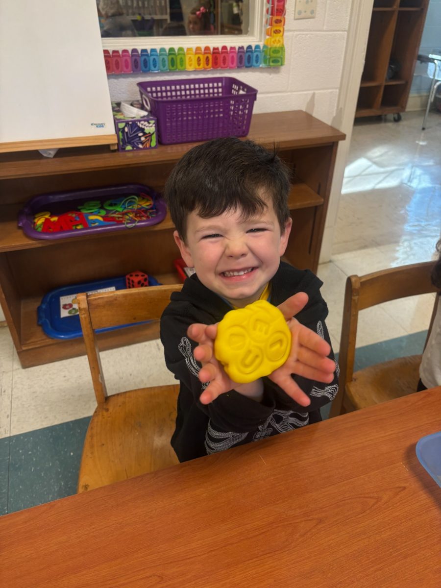 A young boy proudly holding up a yellow craft project at The WEE Center